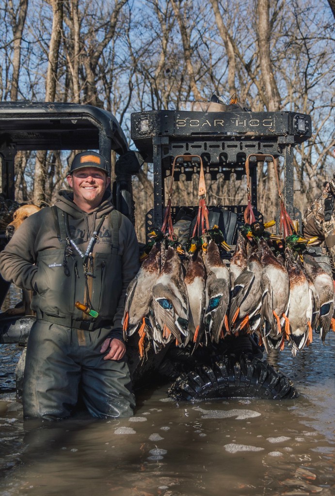 Zane kneeling in flooded timber beside a UTV hung with mallards
